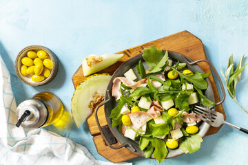 Summer mediterranean salad with melon, bacon, olives, white cheese and arugula on blue stone background. Traditional Spanish and Italian appetizer. View from above. Copy space.