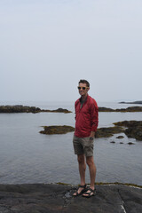 Fototapeta na wymiar man standing on the shoreline in Maine wearing a red jacket - foggy day