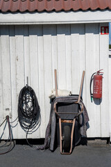 Oslo, Norway, 04.06.2023 a wheelbarrow propped up against a white barn wall, a fire extinguisher and a bundle of black wire cables attached to the white wall