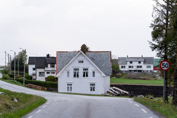 Asphalted light gray road with a white wooden house in front with a gray stone roof above a light bright sky
