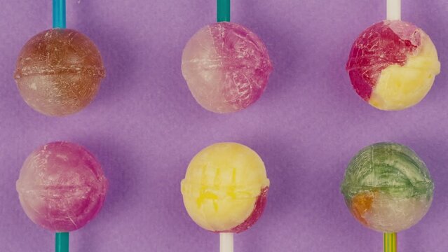 Sweet lollipops with glitter sprinkles on color purple background zoom frame. Bright texture sugar candies close up top view. Composition of favorite children's summer sweets. Studio shot for shop