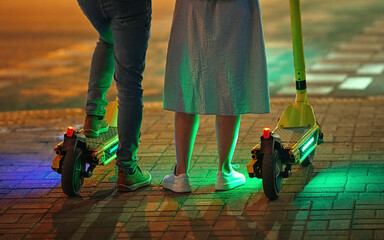 Man and woman riding electric scooter at night. Young couple on electric scooters standing on...