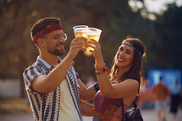 Cheerful couple has fun while toasting with beer on music concert.
