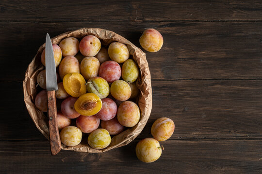 Plums in a paper bag, on wooden table. Top view.
