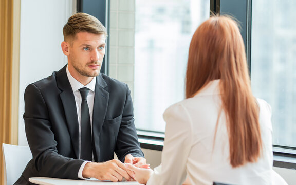 Selective focus caucasian white smart business man wearing formal suit with necktie, seriously talking and discussing with staff, sitting beside window in indoor office.