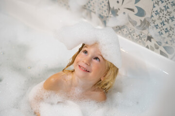 Cute funny caucasian blonde three years old baby girl taking bath with white foam bubbles,child...