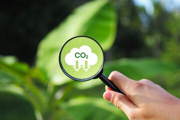 Hand holding a magnifying glass with CO2 reduction icon, no carbon dioxide emissions. Carbon credits to limit global warming.CO2 emission concept. Green industries business concept. Net zero emission.