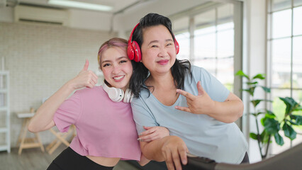 Happy asian elderly women and teenager daughter in sportswear wearing headphones while exercising at home. Smiling and looking at camera. Happy family, Health care concept