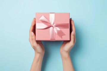 Female hands holding light pink giftbox on the light blue background, top view. Generative AI