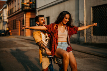 Two couple tourists enthusiastically ride on bicycle, having fun while exploring the city