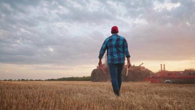 agriculture. farmer walk works in a field next to a tractor that plows the land. business agriculture concept. farmer with tablet works in a field next to a tractor at farm sunset mowed wheat plows