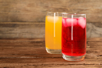 Glasses of different refreshing soda water with ice cubes on wooden table. Space for text