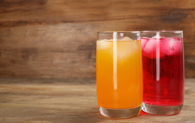 Glasses of different refreshing soda water with ice cubes on wooden table. Space for text