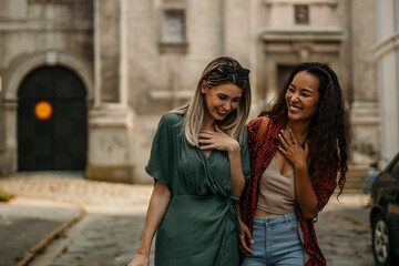 Two diverse females walking through the old city part, holding hands and exploring it. Travel and fashion concept.