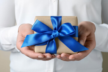 Woman holding gift box with blue bow, closeup
