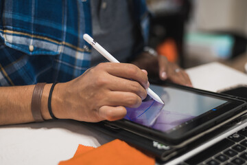 Latin graphic designer working in his office on an illustration tablet, he wears a blue checkered shirt and glasses.