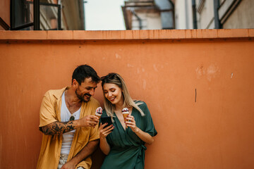 Tourists pose with their ice cream in front of a vibrant wall, using a phone and adding a splash of...
