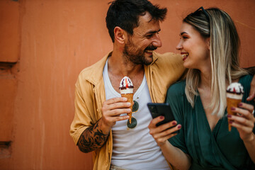 Tourists pose with their ice cream in front of a vibrant wall, using a phone and adding a splash of color to their city exploration.