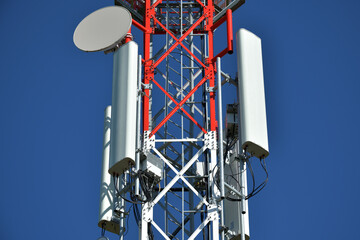 Telecommunication tower with white antenna. Blue sky in background