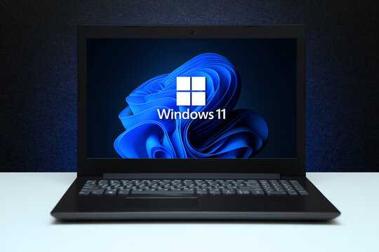 Windows 11 logo on the screen laptop computer on black textured wall with blue light. A new operating system update from Microsoft. Astana, Kazakhstan - July 2, 2023.
