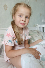 Cute little girl sitting on the bed and smiling. Concept of a leisure