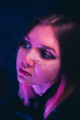 A beautiful young woman with a melancholic expression, adorned with star-shaped makeup, in a club illuminated by pink lights amidst the darkness of the night.