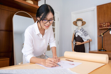 Young female fashion designer sketching at studio desk.