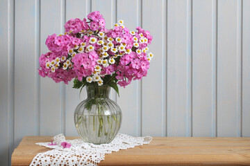 Garden pink phlox and daisies in a glass potbellied vase on a wooden table. Summer.
