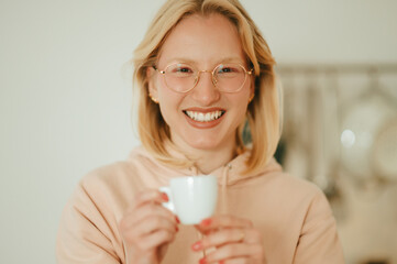 Portrait of a happy blond woman offering cup of morning coffee while smiling at the camera.