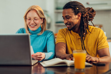 A happy multicultural couple is sitting at their loft and doing home finances on the laptop.