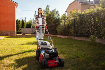 Female gardener working in summer, cutting grass in backyard. Concept of gardening, work, nature. Housework, gardening and country life. Home garden grass cutting woman mowing with lawn mower.
