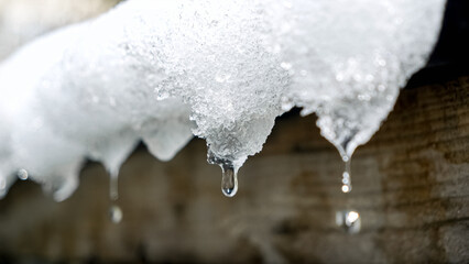 Close-up shot of water droplets falling from icicles on a rooftop. Changing of the seasons,...