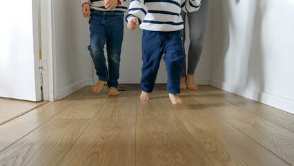 Closeup of playful little boys and their mother's feet running on wooden floor at home. A heartwarming concept of family love and happy childhood memories.