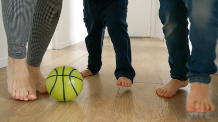 Happy family's feet as they kick a football back and forth on a wooden floor in a house corridor....