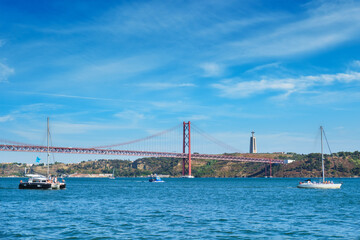 Fototapeta na wymiar View of 25 de Abril Bridge famous tourist landmark over Tagus river, Christ the King monument and a tourist yacht boat. Lisbon, Portugal
