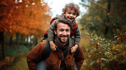 Father giving son ride on back in park. Portrait of happy father giving son piggyback ride on his shoulders and looking up. Cute boy with dad playing outdoor.