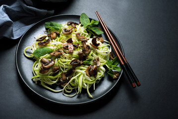 Zucchini pasta with mushrooms and mint on a dark background. Delicious organic vegan food