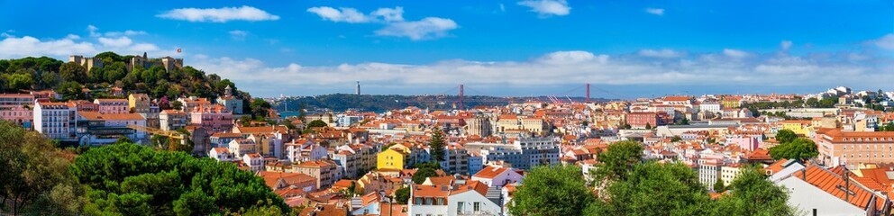 Lisbon famous panorama from Miradouro dos Barros tourist viewpoint over Alfama old district with St. George's Castle, Portugal flag, 25th of April Bridge, Christ the King statue. Lisbon, Portugal.