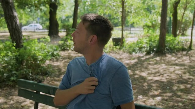 Man suffering from heat wave Cerberus in South Europe. Caucasian male presses bottle of water to face to cool off suffering from heat sitting in the shadow outdoors