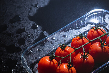 fresh tomatoes in plastic packaging on a black background with water drops