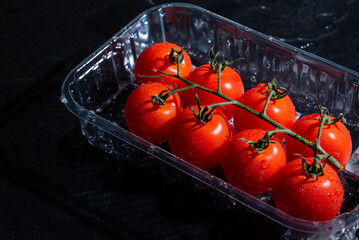 fresh tomatoes in plastic packaging on a black background with water drops