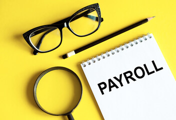 Business flat lay with the inscription PAYROLL on notepad. Yellow background