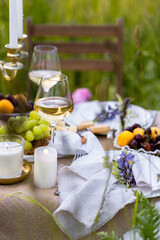 Elegant fancy wedding table decor with bright ranunculi flowers in a vase outdoors, chandelier, field or meadow. Summer, sunset, golden hour. Romantic dinner for a couple in restaurant outside