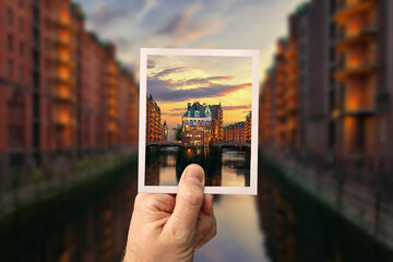 Hand with instant photo picture of the Speicherstadt in the foreground and the actual unsharp...