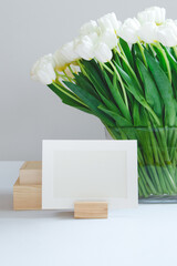 Folio photo frame in a wooden holder with a bouquet of white tulips on the background
