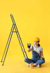 Female decorator with cans of paint and stepladder on yellow background