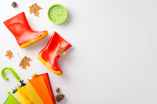 Vibrant rainy day theme for kids in autumn. Photograph a top-down view of a vivid scene featuring a colorful umbrella and red rubber boots on a white backdrop, leaving space for text or advertising