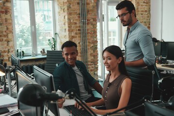Daily routine. Group of young employees working on computers and discussing project results while...