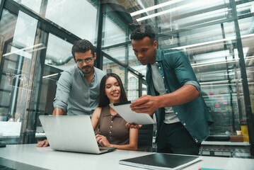 Searching for solutions. Group of three young and positive employees using modern technologies and...