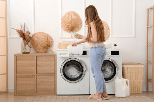 Woman adding detergent into washing machine in laundry room
